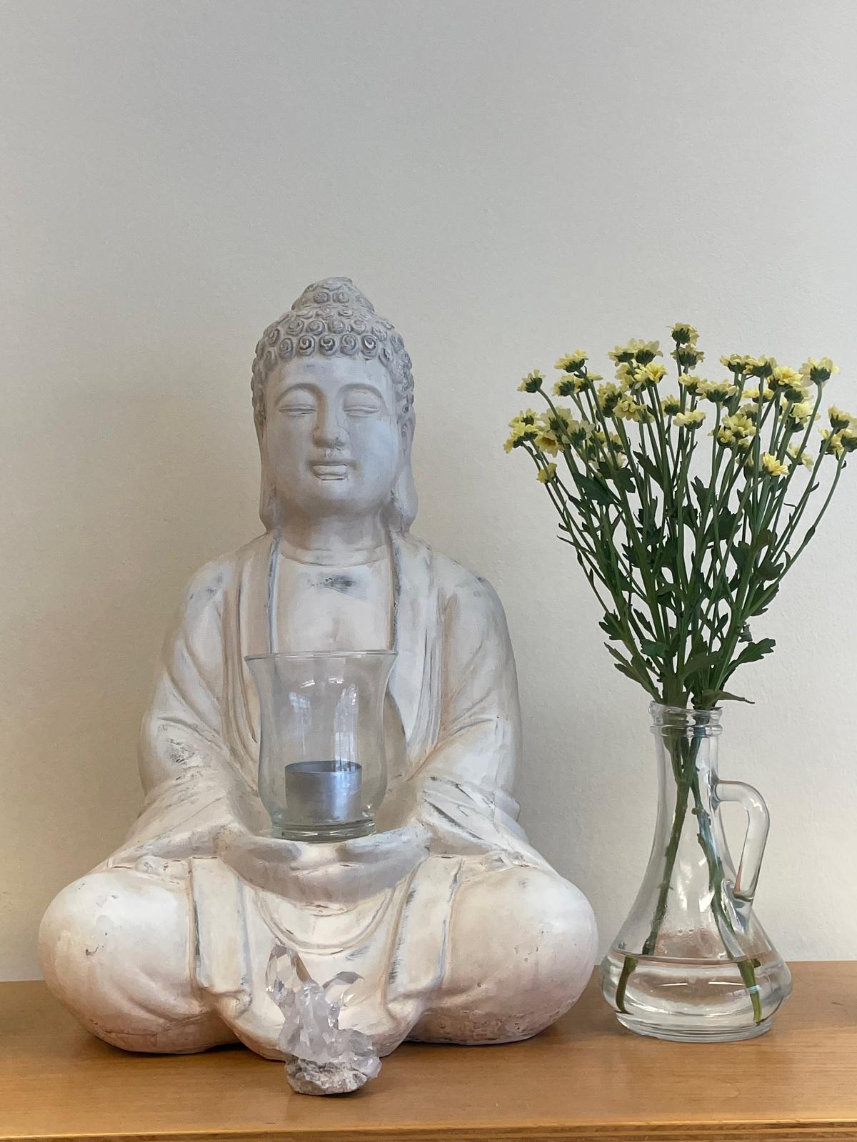 Buddha-Figur mit Bergkristall und frischen Blumen im Salon